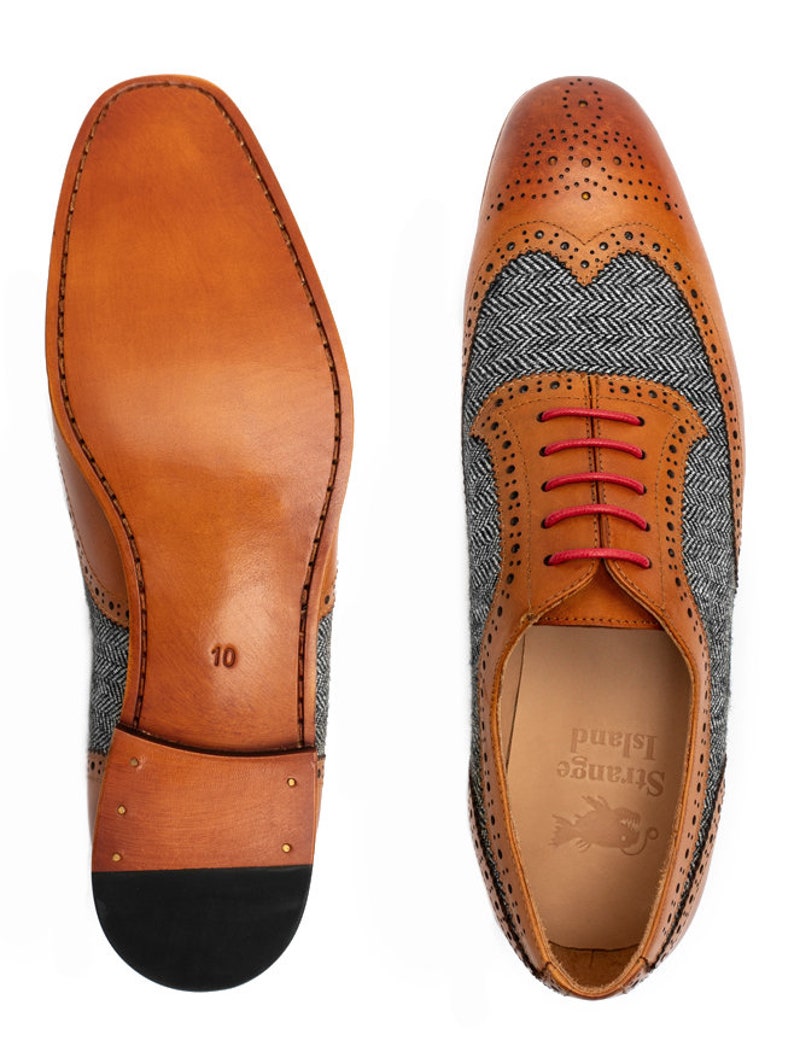 May include: A pair of brown leather shoes with a grey tweed pattern on the sides. The shoes have red laces and a black sole. The shoes are size 10 and have the brand name "Strange Island" on the inside.