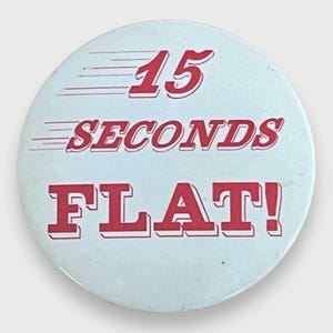 Può includere: Un bottone rotondo azzurro con testo rosso "15 SECONDS FLAT!". Il testo è in grassetto, bordato di bianco e con linee di velocità. Design vintage.