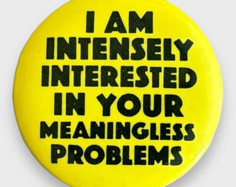 May include: A round, yellow button with black text. The text reads: "I AM INTENSELY INTERESTED IN YOUR MEANINGLESS PROBLEMS."