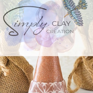 May include: A brown ceramic angel figurine with a glittery finish and a detailed patterned base. The angel has a blue and gold butterfly on its wing. The text "simply CLAY CREATION" is visible in the background.