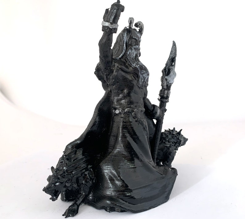 Puede incluir: Una figura miniatura en negro y plata de una figura que lleva una corona y una t&uacute;nica, sosteniendo un bast&oacute;n y de pie sobre dos lobos.