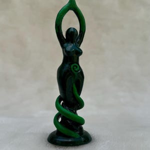 May include: Green goddess statue with a spiral design and raised arms. The statue is made of a dark green material and stands on a base.