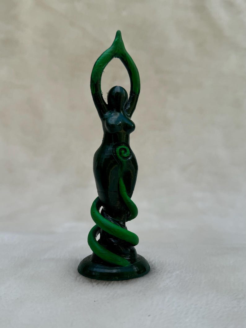 May include: Green goddess statue with a spiral design and raised arms. The statue is made of a dark green material and stands on a base.