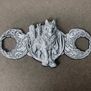 May include: A silver-toned metal pendant featuring a wolf design with intricate details. The wolf is standing on a crescent moon with a floral pattern. The pendant is attached to a chain.