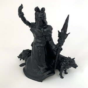 Puede incluir: Figurilla impresa en 3D en blanco y negro de una figura femenina con el pelo largo y un bast&oacute;n, de pie sobre dos lobos.