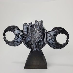 May include: A black and silver 3D printed sculpture of a wolf standing on a crescent moon. The wolf is surrounded by a decorative design of leaves and vines. The sculpture is mounted on a black wooden base.