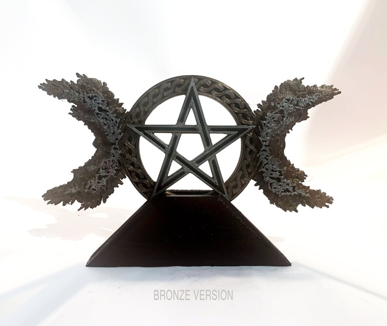 May include: A bronze pentagram with a Celtic knot design, surrounded by two crescent moons, on a black triangular base. The base has the text "BRONZE VERSION" printed on it.