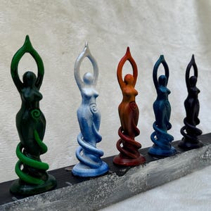 May include: Five small, colourful statues of women with swirling bases. The statues are green, white, orange, blue, and black.