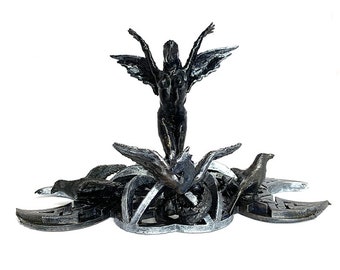 May include: A black metal sculpture of a winged figure standing on a base with three birds. The base is decorated with a Celtic knot design.
