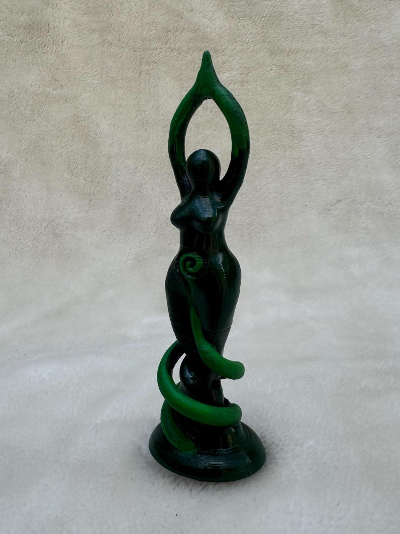 May include: Green goddess statue with arms raised in a pose of worship. The statue is made of a dark green material and has a swirling design.