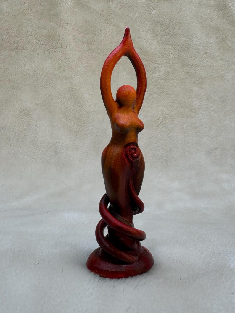 May include: A red and orange wooden sculpture of a woman with her arms raised above her head. The sculpture is standing on a base with a spiral design.