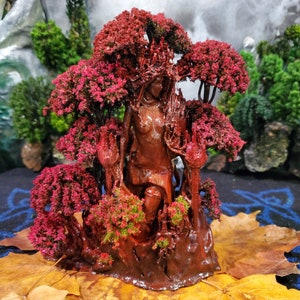 May include: A red resin sculpture of a female figure standing in a forest setting. The figure is surrounded by trees and vines, and the base of the sculpture is covered in moss.