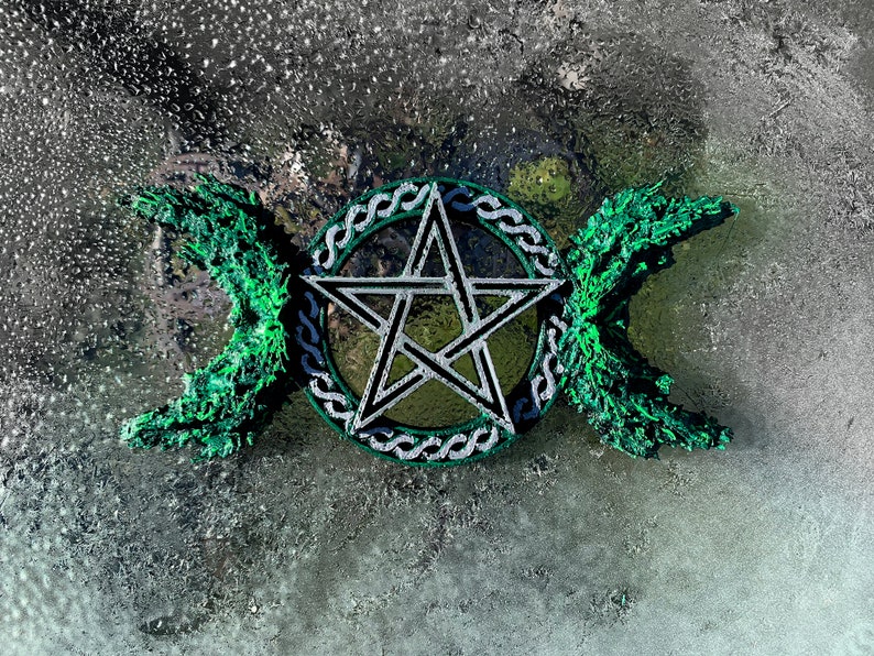 May include: A silver pentacle with a green triple moon symbol on a gray background.