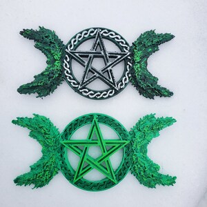 May include: Two triple moon pentagram wall decor pieces. One is silver with a green background and the other is green with a green background.