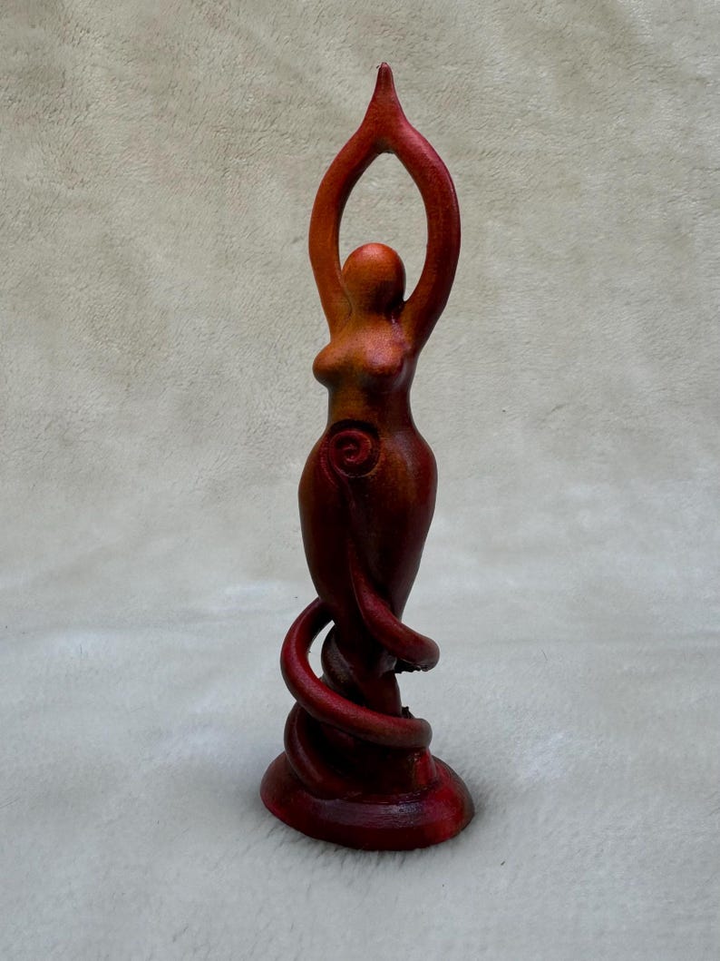 May include: A wooden sculpture of a woman with her arms raised, painted in shades of red and orange. The sculpture has a spiral design on the woman's abdomen.