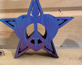 May include: A wooden star-shaped ornament painted in shades of blue and purple with a peace sign cut out in the centre.