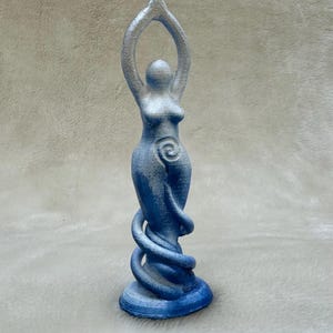 May include: A blue and silver ceramic statue of a woman with her arms raised in the air. The statue has a spiral design on the front and a base that is shaped like a snake.