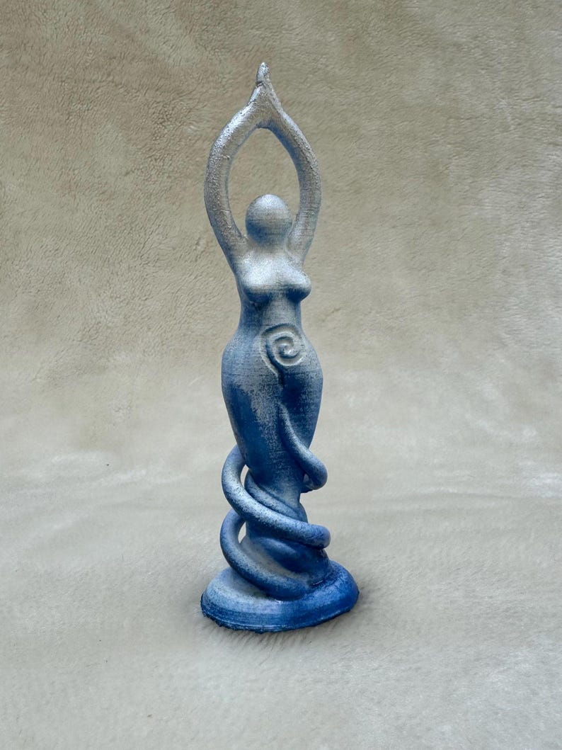 May include: A blue and silver ceramic statue of a woman with her arms raised in the air. The statue has a spiral design on the front and a base that is shaped like a snake.