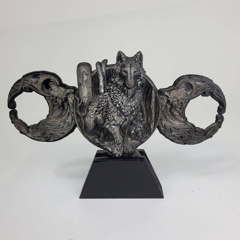 May include: A silver-colored sculpture of a wolf standing on a black base. The wolf is surrounded by a decorative design of swirling lines and shapes. The sculpture is a unique and eye-catching piece of art.