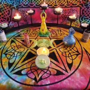 May include: A pentagram with a green and yellow goddess statue in the center, surrounded by candles and other ritual items on a colorful mandala tablecloth.