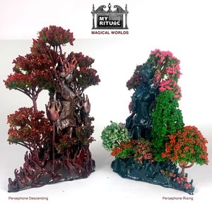 May include: Two 3D printed figurines of a woman standing in a forest setting. The figurine on the left is in a dark red forest with a fiery red base. The figurine on the right is in a dark blue forest with a dark blue base. The text "MY RITUAL MAGICAL WORLDS" is at the top of the image. The figurine on the left is labeled "Persephone Descending" and the figurine on the right is labeled "Persephone Rising".