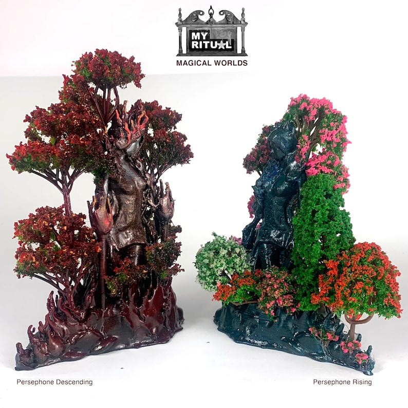 May include: Two 3D printed figurines of a woman standing in a forest setting. The figurine on the left is in a dark red forest with a fiery red base. The figurine on the right is in a dark blue forest with a dark blue base. The text "MY RITUAL MAGICAL WORLDS" is at the top of the image. The figurine on the left is labeled "Persephone Descending" and the figurine on the right is labeled "Persephone Rising".