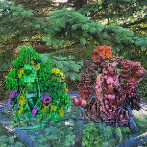 May include: Two 3D printed sculptures of figures standing in a forest setting. The figure on the left is green and surrounded by green and yellow foliage. The figure on the right is red and surrounded by red and brown foliage.
