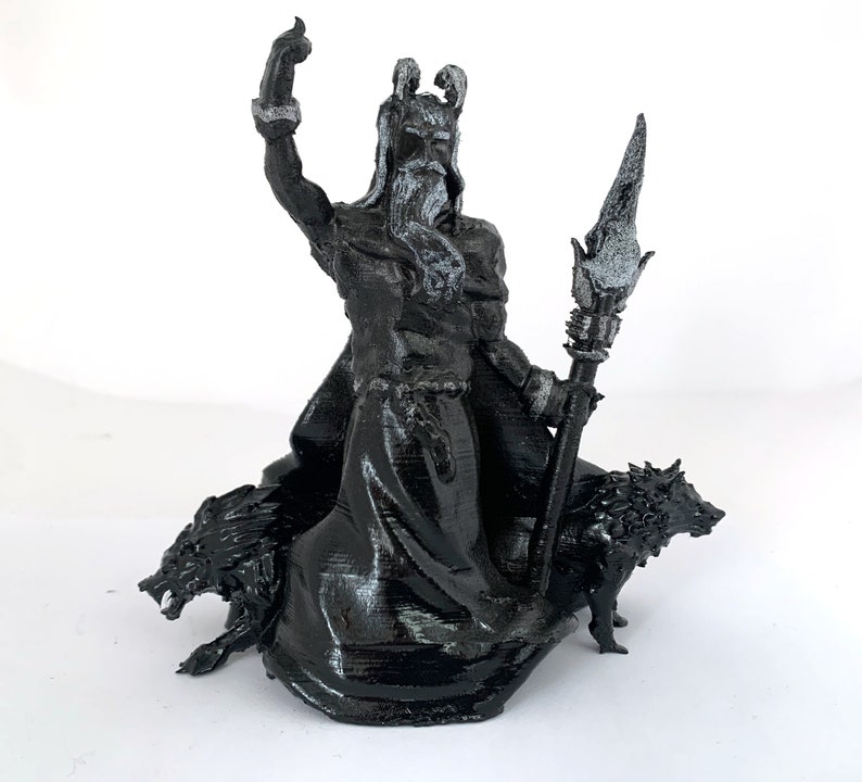 Puede incluir: Una figura impresa en 3D en blanco y negro de una figura m&iacute;tica con una larga barba y una corona, sosteniendo un bast&oacute;n y montando dos lobos.