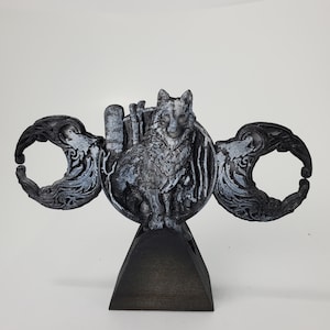 May include: A black and silver 3D printed sculpture of a wolf standing on a crescent moon. The wolf is surrounded by a decorative design of leaves and vines. The sculpture is mounted on a black wooden base.