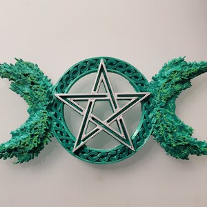 May include: A green and silver pentagram with a triple moon symbol on either side. The pentagram is surrounded by a circle with a Celtic knot design.