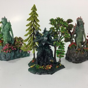 May include: Three miniature figurines of green-skinned creatures standing on bases with small trees and flowers. The creatures are posed in different positions, and the bases are decorated with green, brown, and pink paint.