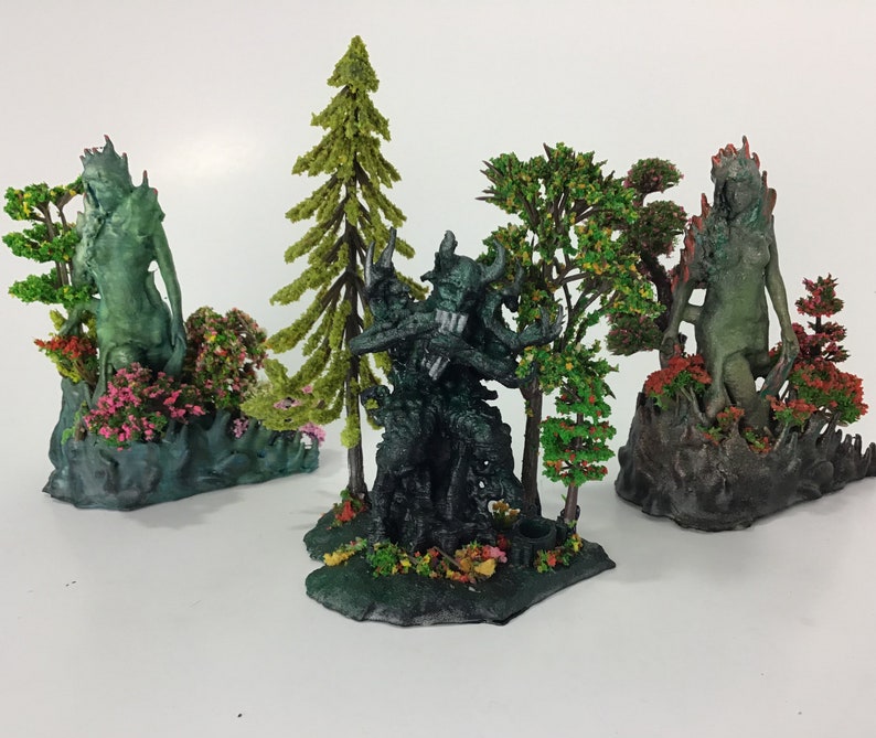 May include: Three miniature figurines of green-skinned creatures standing on bases with small trees and flowers. The creatures are posed in different positions, and the bases are decorated with green, brown, and pink paint.