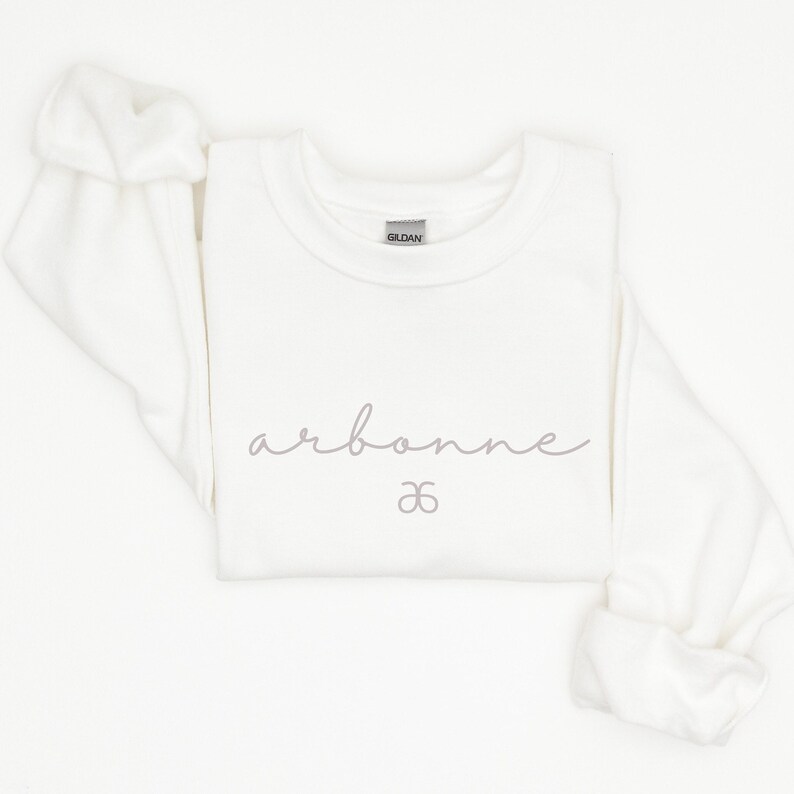 May include: White crewneck sweatshirt with the word "arbonne" and a infinity symbol printed in gray on the front.