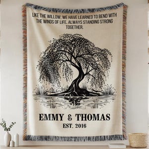 May include: Cream-colored woven throw blanket featuring a black illustration of a weeping willow tree reflected in water. The text "LIKE THE WILLOW, WE HAVE LEARNED TO BEND WITH THE WINDS OF LIFE, ALWAYS STANDING STRONG TOGETHER." is at the top. Below the tree is the text "EMMY & THOMAS EST. 2016."
