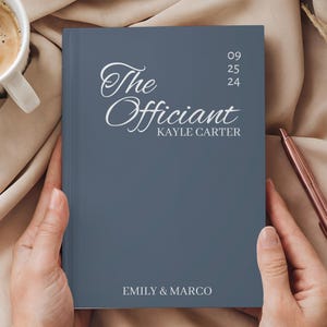 Puede incluir: Un cuaderno azul titulado "The Officiant" con el nombre Kayle Carter y la fecha 09/25/24. Los nombres "Emily & Marco" están impresos en la parte inferior. Una taza de café y un bolígrafo también están en la imagen.