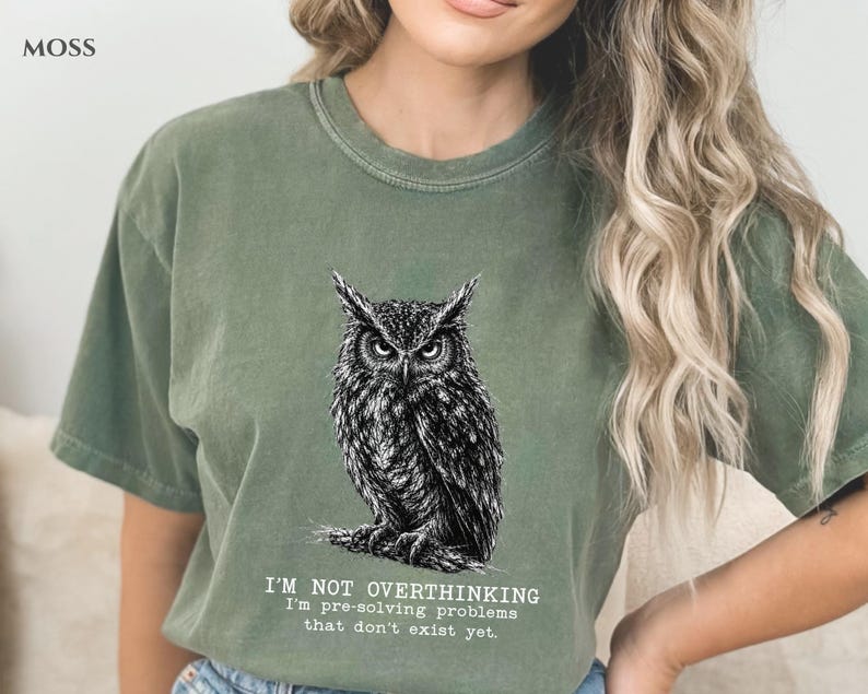 Puede incluir: Una camiseta de manga corta color verde musgo con una ilustraci&oacute;n detallada en blanco y negro de un b&uacute;ho posado en una rama. Debajo del b&uacute;ho, el texto dice: I'M NOT OVERTHINKING I'm pre-solving problems that don't exist yet. Cuello redondo.