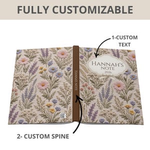 May include: Open notebook with a floral design featuring pink, purple, and yellow flowers on a beige background. The text "Hannah's Note 2026" is displayed on the cover. The spine is brown and labeled "Hannah's Note". The text "FULLY CUSTOMIZABLE" is at the top.