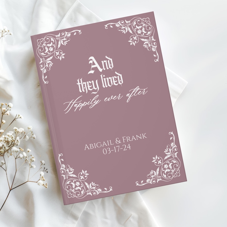 May include: A mauve-colored book with the text "And they lived Happily ever after" in white script. The names "ABIGAIL & FRANK" and the date "03-17-24" are also printed on the cover. White floral corner designs add a decorative touch.