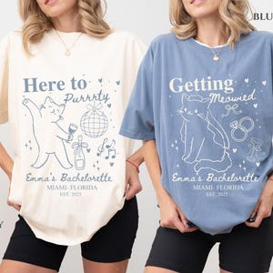 Puede incluir: Dos camisetas, una marfil y otra azul, con dise&ntilde;os de despedida de soltera con tem&aacute;tica de gatos. La camiseta marfil dice "Here to Purrrty" con un gr&aacute;fico de gato, mientras que la camiseta azul dice "Getting Meowied". Ambas camisetas incluyen "Emma's Bachelorette" y la ubicaci&oacute;n y el a&ntilde;o.