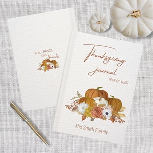 May include: A Thanksgiving journal with a brown cover and a white background. The cover features a watercolor illustration of pumpkins, fall leaves, and flowers. The text "Thanksgiving journal" is written in brown cursive script. The text "Year by Year" is written in brown text below the title. The text "The Smith Family" is written in brown text at the bottom of the cover.