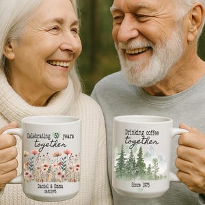 Może przedstawiać: Dwa białe ceramiczne kubki z uchwytami. Jeden kubek m&oacute;wi "Celebrating 50 years together" z kwiatowym wzorem i imionami. Drugi kubek m&oacute;wi "Drinking coffee together" ze sceną leśną i rokiem 1975.