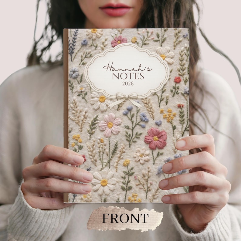 May include: A floral-embroidered notebook with the text "Hannah's NOTES 2026" on the cover. The notebook features a cream-colored background with colorful embroidered flowers. The word "FRONT" is printed at the bottom.