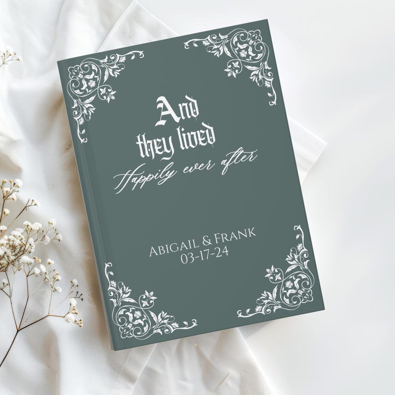 May include: A hardcover book with a teal cover featuring the text "And they lived happily ever after." The book has decorative white floral corner designs and the names "ABIGAIL & FRANK" with the date "03-17-24" printed on the cover.