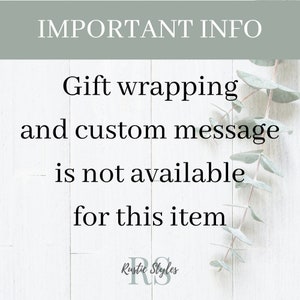May include: A white wooden sign with the text "IMPORTANT INFO" in black lettering. The sign also includes the text "Gift wrapping and custom message is not available for this item" in black lettering. The sign is decorated with eucalyptus leaves.