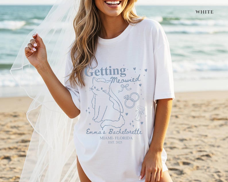 Puede incluir: Camiseta blanca con una ilustraci&oacute;n de gato azul claro y el texto "Getting Meowied". La camiseta tambi&eacute;n incluye el texto "Emma's Bachelorette, Miami-Florida, Est. 2023". Tema de despedida de soltera.