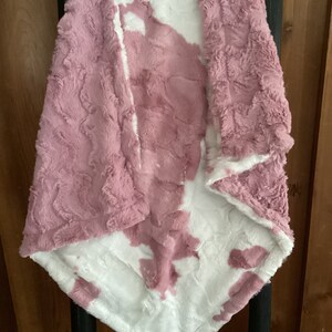 May include: A soft, plush blanket with a pink and white tie-dye pattern. The blanket is made of a fluffy, fuzzy material and is perfect for cuddling up on the couch.
