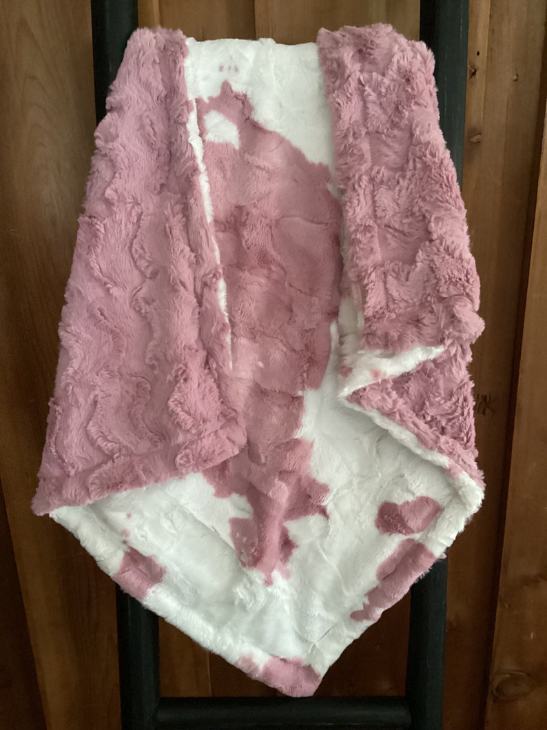 May include: A soft, plush blanket with a pink and white tie-dye pattern. The blanket is made of a fluffy, fuzzy material and is perfect for cuddling up on the couch.