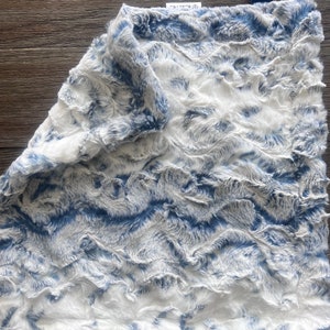 May include: A soft, blue and white plush blanket with a wavy pattern. The blanket has a tag that says "Little Love Co."