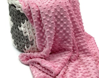 May include: A soft pink blanket with a raised dimpled texture draped over a round storage basket made of thick, braided white and gray rope. The blanket features a consistent pattern of small, rounded bumps across its entire surface.
