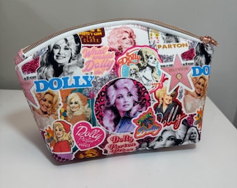 May include: A trapezoidal cosmetic bag featuring a collage of Dolly Parton photographs, pink glitter accents, and text including Dolly, What would Dolly do?, and Dolly Parton vibes. The bag has a rose gold zipper closure along the top edge.